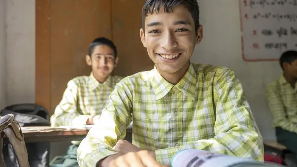 Child smiles while sitting at his desk in middle school in India