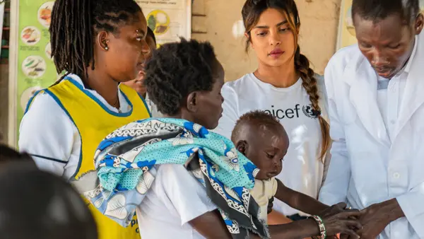 Brenda Ekiru holds her 10-month-old son, Kevin, as he gets a medical check-up from a health officer while UNICEF Goodwill Ambassador Priyanka Chopra Jonas, center, looks on.