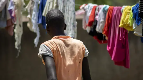 An adolescent girl looks at laundry hanging on clotheslines, her back turned to the camera
