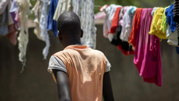 An adolescent girl looks at laundry hanging on clotheslines, her back turned to the camera