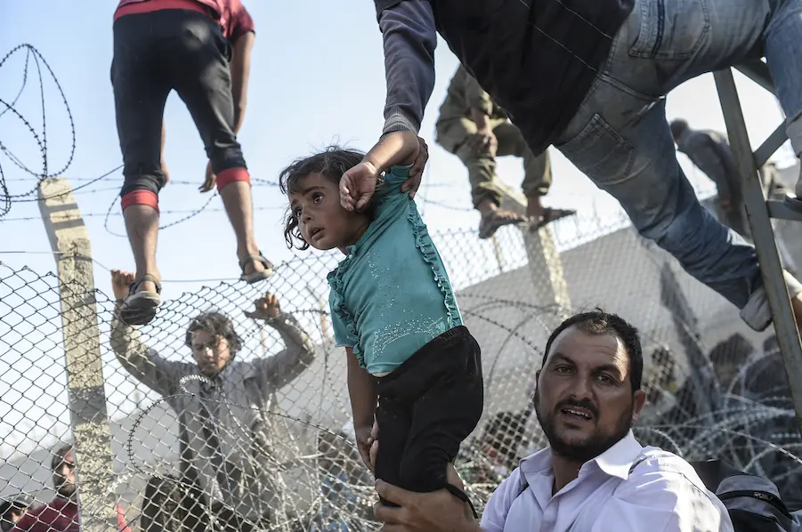 Syrian refugees cross into Turkey through a broken fence near the official border crossing at Akçakale on June 14, 2015. Syrian refugees cross into Turkey through a broken fence near the official border crossing at Akçakale on June 14, 2015.