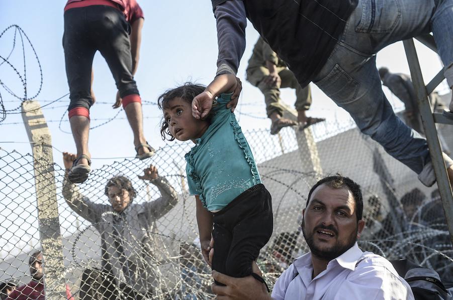 Syrian refugees cross into Turkey through a broken fence near the official border crossing at Akçakale on June 14, 2015. 