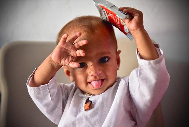 In Pakistan, 10-month-old Younas holds a packet of Ready-to-Use Therapeutic Food (RUTF).