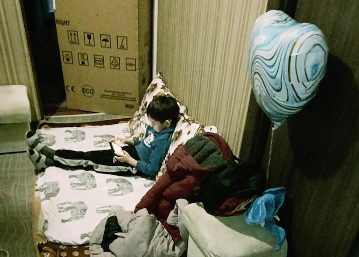 7-year-old Maksim sat on the floor of his family's apartment in Mariupol with packed suitcases nearby.