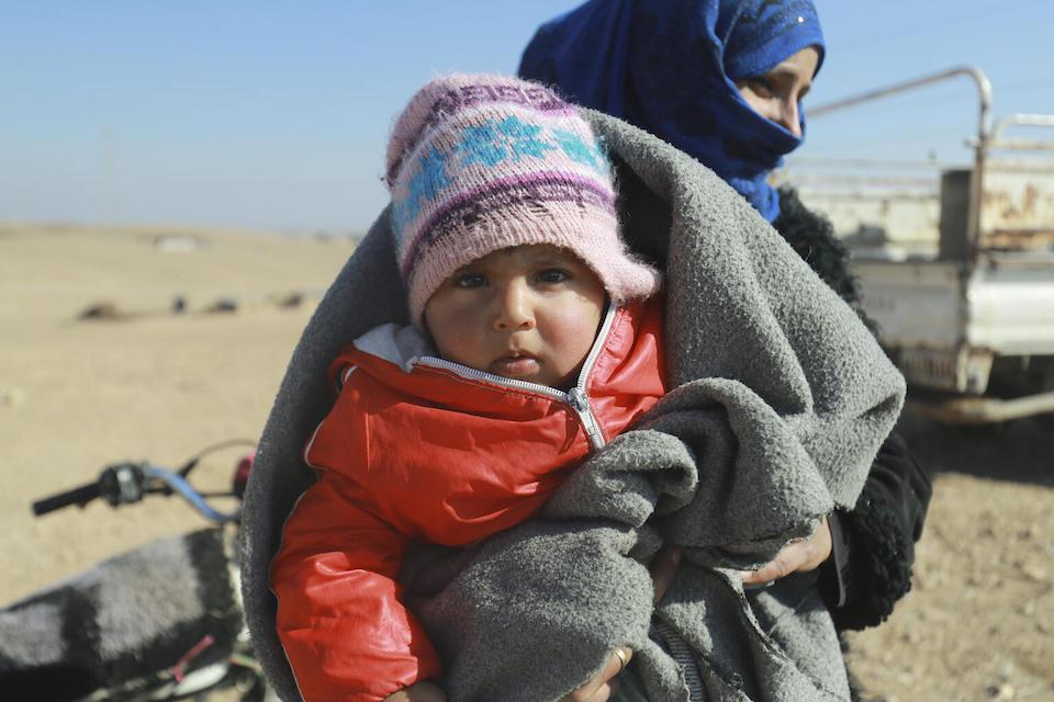 A baby is held by her mother as the family waits to receive a winter kit, distributed by UNICEF, in northeast Syria.