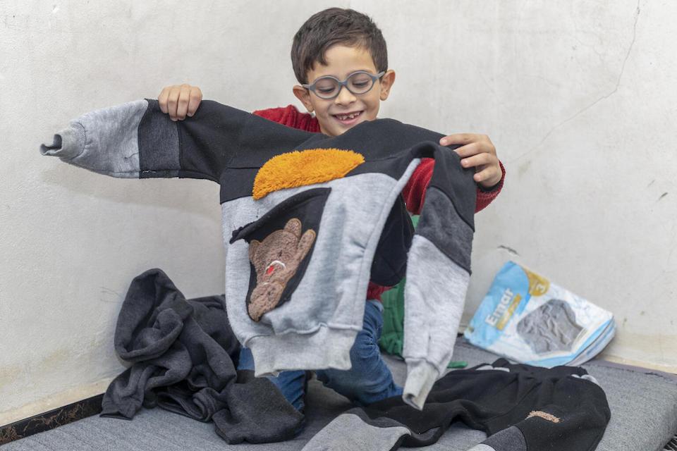 A boy holds up his new winter sweater at his home in Aleppo, Syria. The sweater was bought with cash for winter assistance provided by UNICEF.