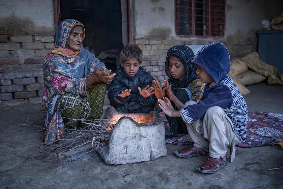 A woman and her grandchildren try to to keep themselves warm around a stove at their home in Dadu District, Sindh Province, Pakistan.