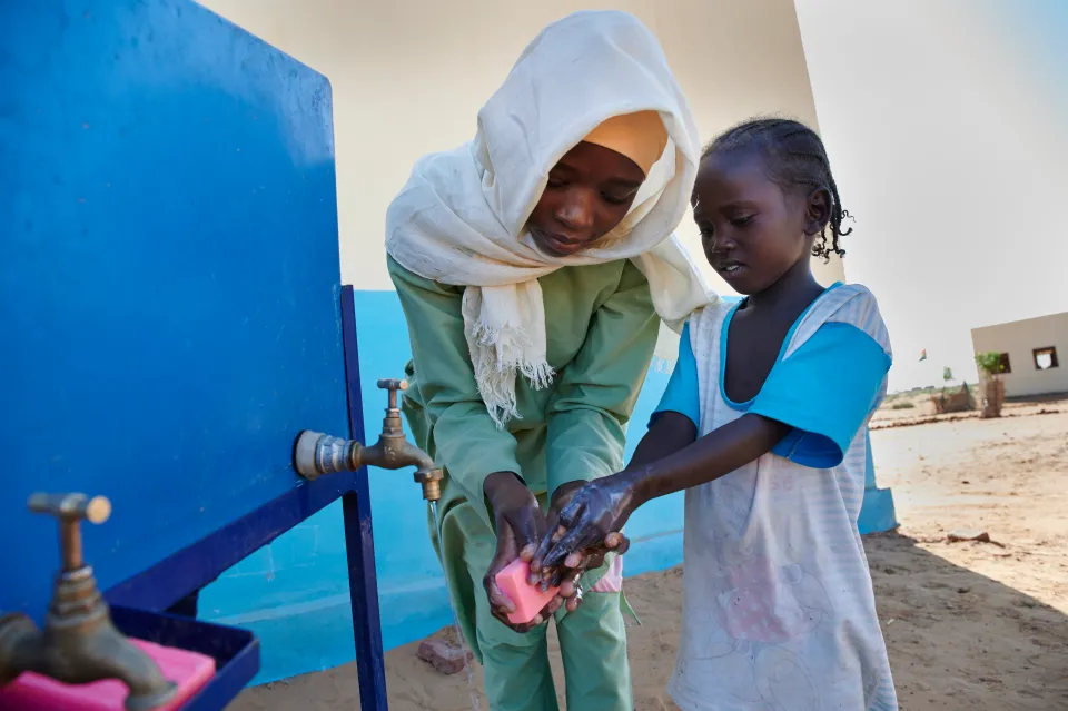An older girl child shows a Kindergarten student how to properly wash her hands using soap and water outside the Ban Jadid Primary School in El-Fasher, the capital of North Darfur, Sudan.