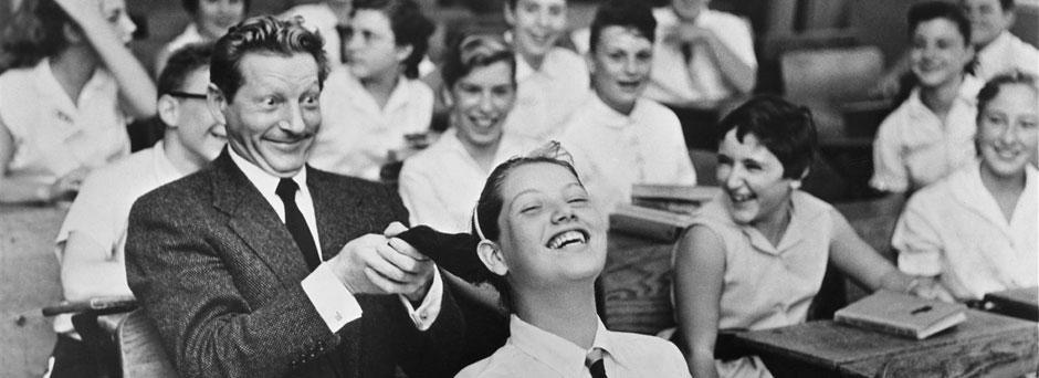 UNICEF Goodwill Ambassador Danny Kaye playfully pulls the hair of a girl seated in front of him, in a classroom filled with laughing children, during a visit to his primary-school alma mater, Public School 149 in the borough of Brooklyn in New York City.