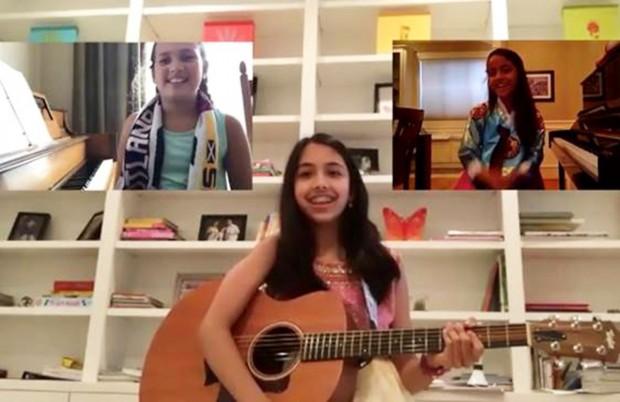 smiling girl holding a guitar with two other smiling girls on video conference