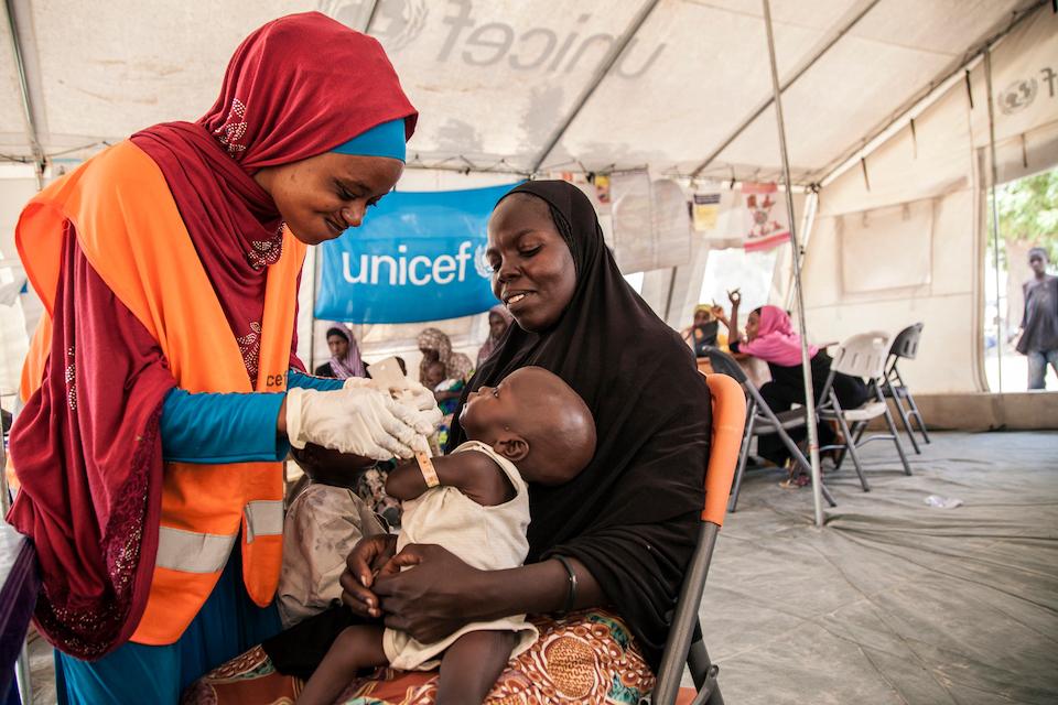 UNICEF Nutrition Officer, Aishat Abdullahi, assesses 7-month-old Umara Bukar for malnutrition at a UNICEF-supported health clinic at Muna Garage displacement camp, Maiduguri, Borno State, northeast Nigeria as Umara’s mother (in black) looks on.