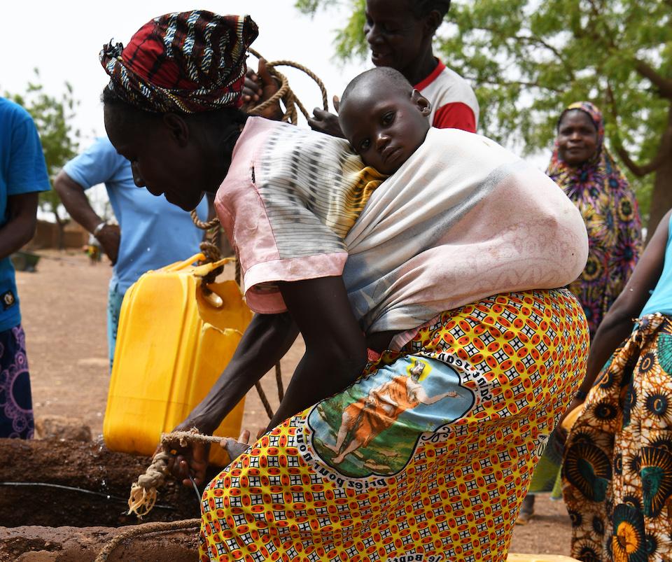 With her baby on her back, a woman in the village of Song Naba, Passoré province, northern Burkina Faso, gathers water from a community source...