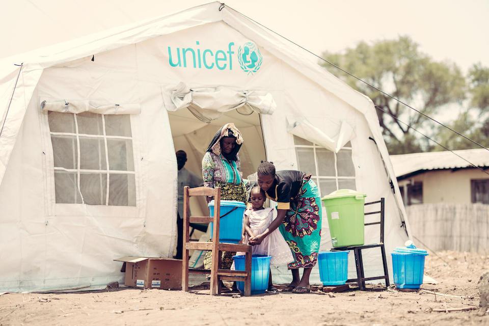 Two-year-old Gladys and her mother Mary wash their hands outside a UNICEF-supported health facility in rural Chilumbra, Karonga district, northern Malawi, as another member of the community looks on.