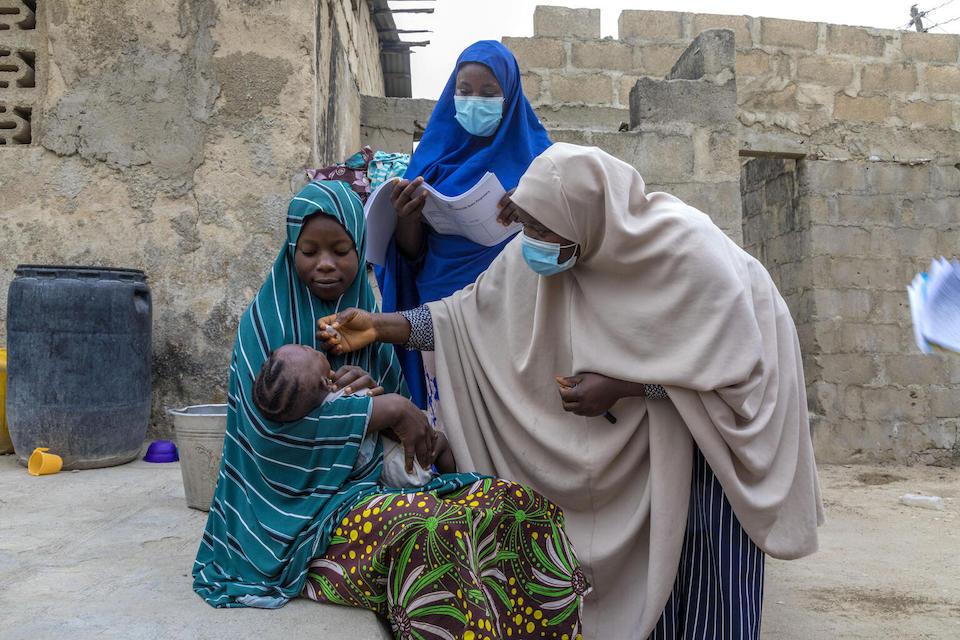 Volunteer community mobilizer Najaatu Musa, center, watches as a member of her team vaccinates 6-month-old Amina during a house-to-house routine vaccination campaign in Minna, Niger State, north-central Nigeria. 