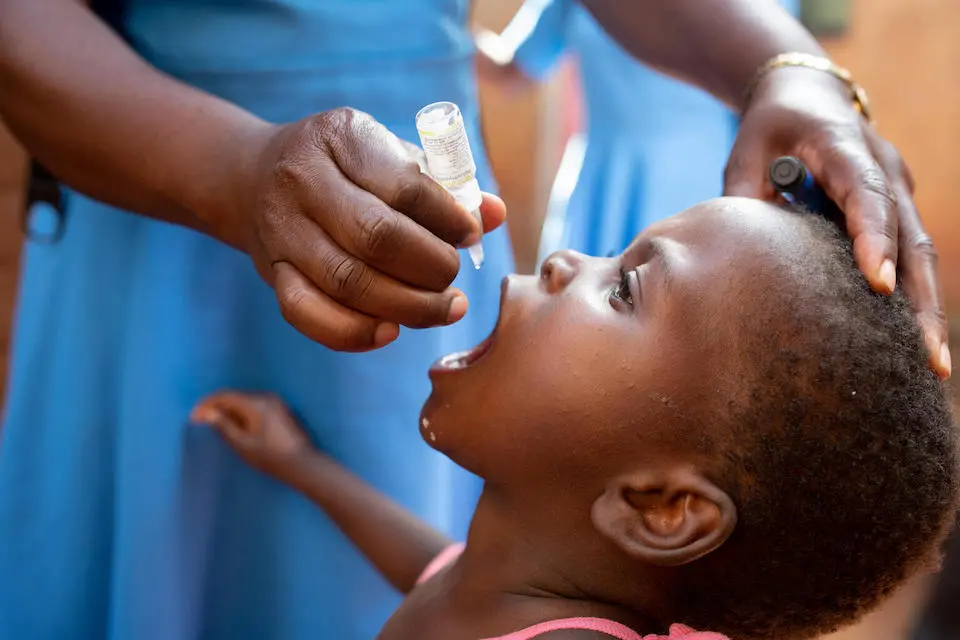 On April 25, 2022, in Lilongwe, Malawi, Matilda Mlumpwa, a health surveillance assistant with the Malawi Ministry of Health, administers the polio vaccine to 3-year old Maria Mphetso as part of a UNICEF-supported door-to-door immunization campaign.