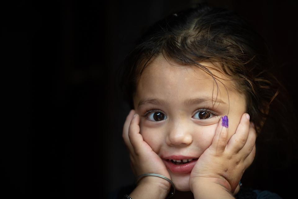 A 4-year-old girl in Karachi, Pakistan, smiles while showing her finger marked in purple ink to show she has received her polio vaccine.