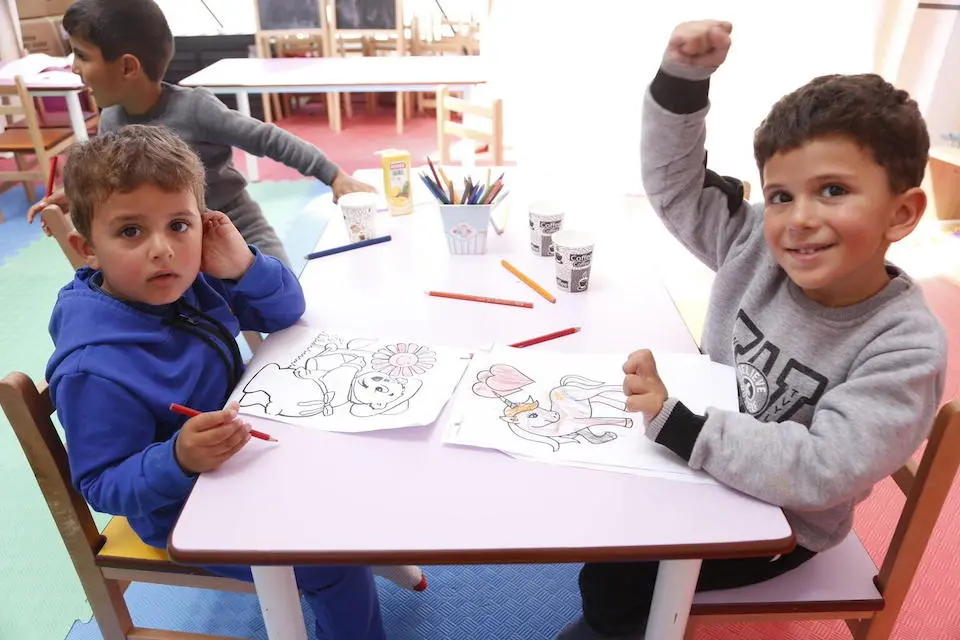 Two young boys displaced by devastating earthquakes sit at a drawing table at a UNICEF-supported Child-Friendly Space in Hatay, Türkiye.