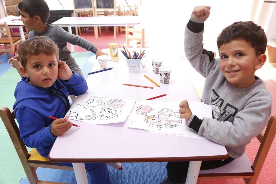 Two young boys displaced by devastating earthquakes sit at a drawing table at a UNICEF-supported Child-Friendly Space in Hatay, Türkiye.