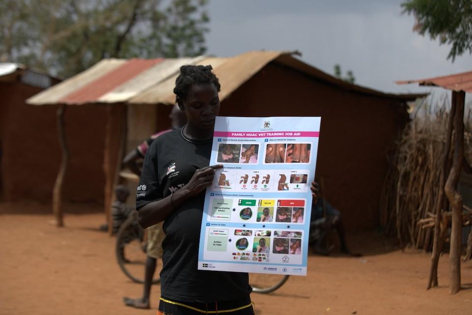 A community volunteer holds up a sign that teaches warning signs of malnutrition.