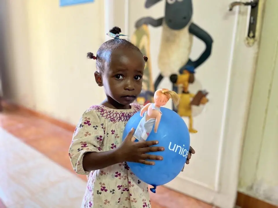 A young girl holds a doll and a balloon inside a child-friendly space established in April 2023 at the Karkar bus station in Aswan, Egypt, to provide psychosocial support to refugee children displaced by conflict in Sudan.