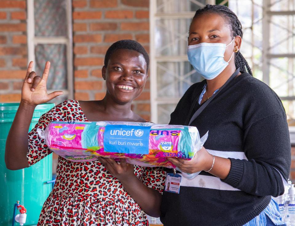 Marie, 20, of Rwanda poses with the supply distributor and new packages of menstrual pads procured and delivered by UNICEF.