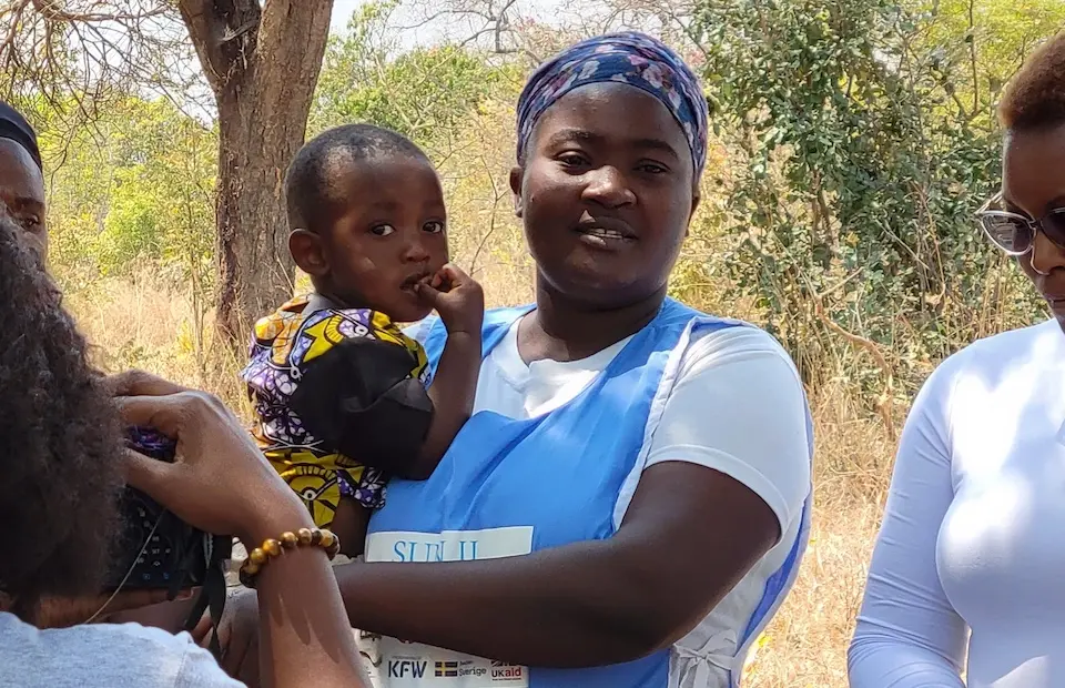 A volunteer holds a young child during a UNICEF-supported community event in rural Zambia offering health and nutrition services to families in need.