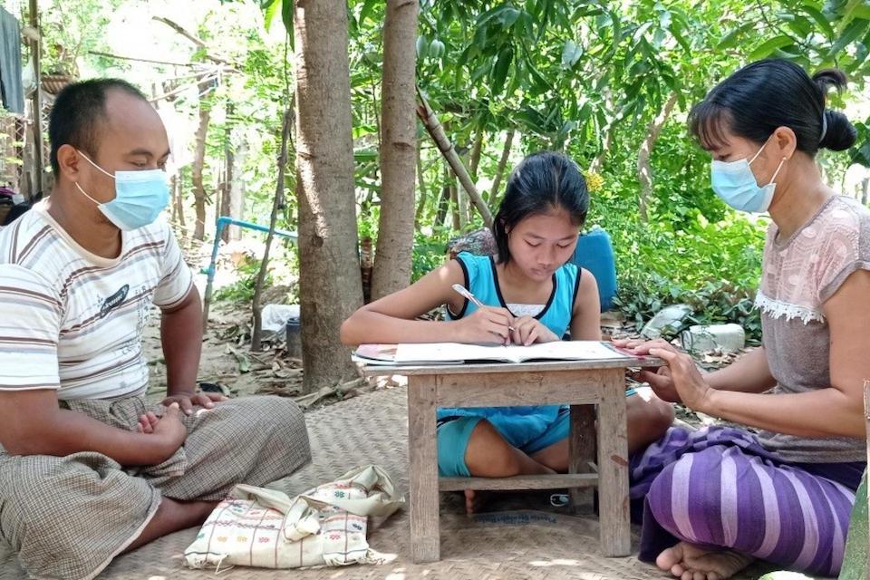 Win Lei, 12, of Myanmar, doing schoolwork as her parents look on. 