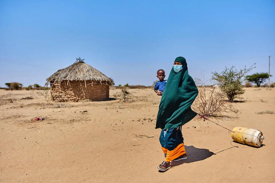 Nasri Garane carries 2-year-old son Liban Ali on her way to a water kiosk in Daley Village, Garissa County.