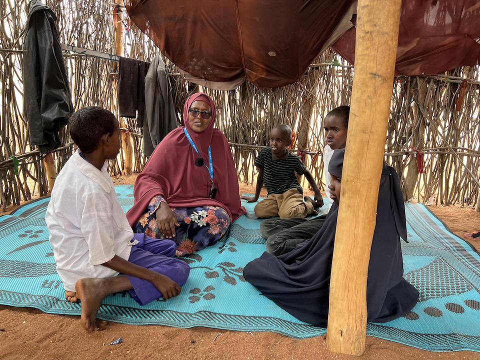 UNICEF child protection specialist sits on a blanket during a visit with children whose parents left with the family's livestock to find fodder and water for the animals.