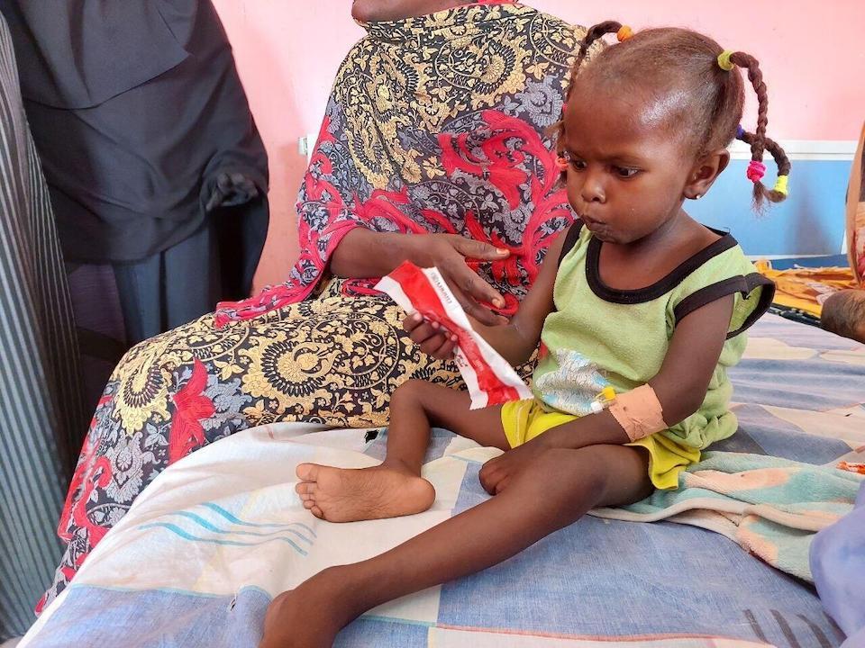 A 3-year-old girl recovering from severe acute malnutrition sits on her hospital bed holding a packet of Ready-to-Use Therapeutic Food, provided by UNICEF. 