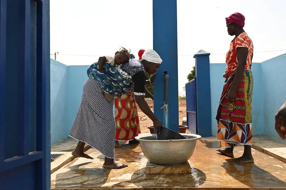 A woman carrying a child collects water from a community tap in the village of Nambekaha, north Côte d’Ivoire.