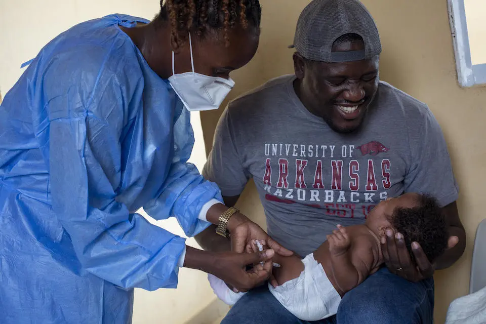Two-month-old Kailane is held by her father, Wilson Abreu, while nurse Quénia Pinto administers a vaccine in Angola.