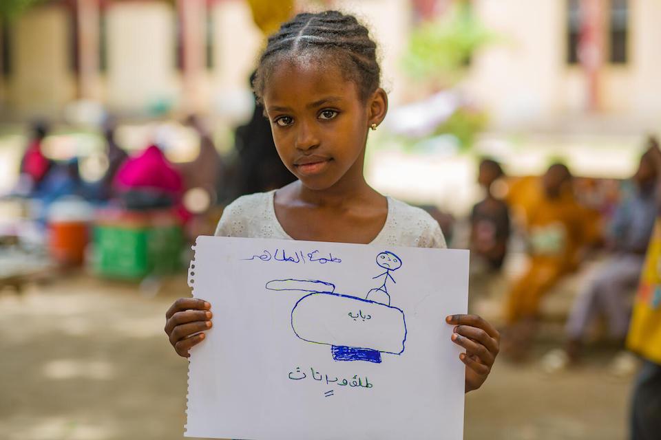 On June 3, 2023, Fatima displays her drawing of a tank during psychosocial activities at a UNICEF-supported gathering center for the displaced in Madani, Sudan.