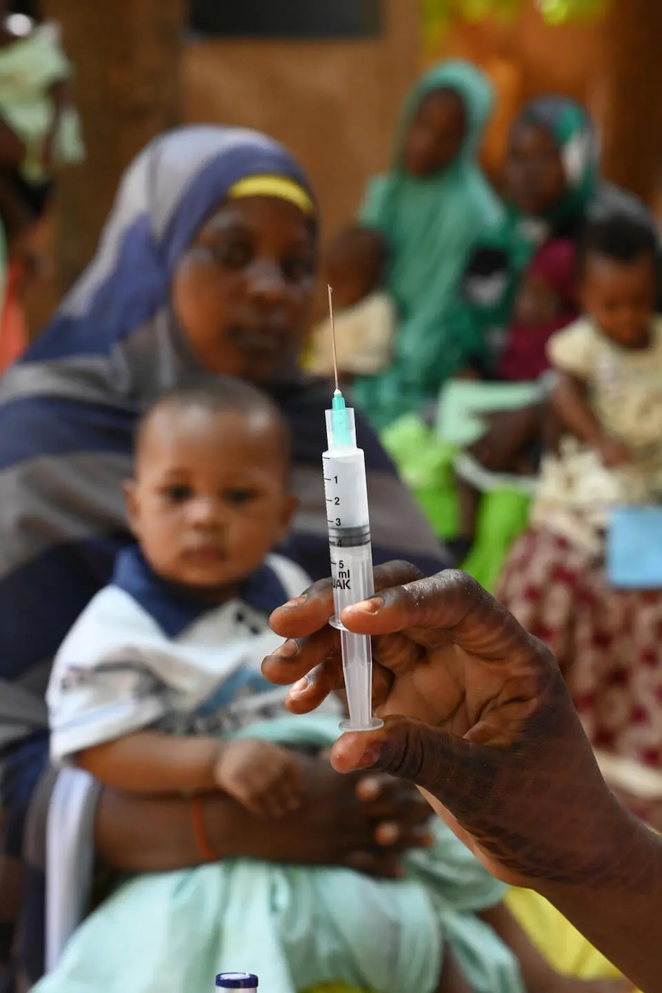 A woman and her baby look at a hand holding a syringe