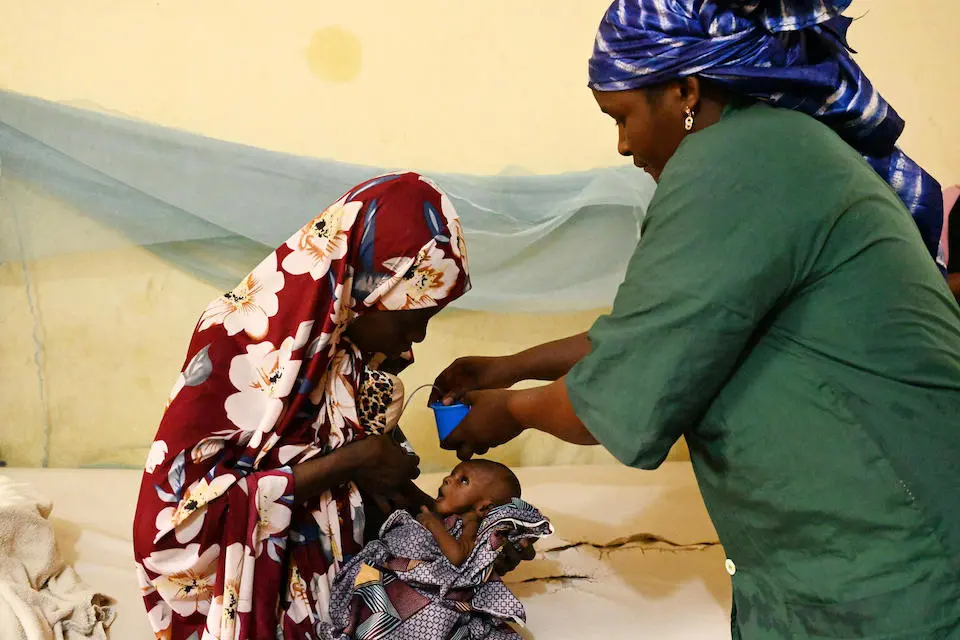 A mother holds her baby while a woman gives an oral vaccine