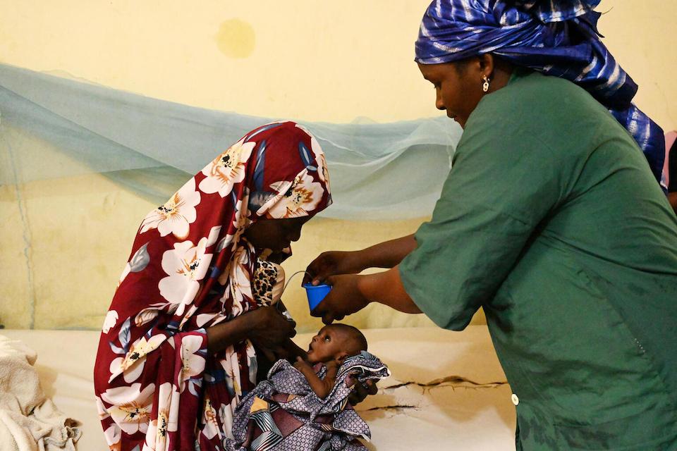 A mother holds her baby while a woman gives an oral vaccine 