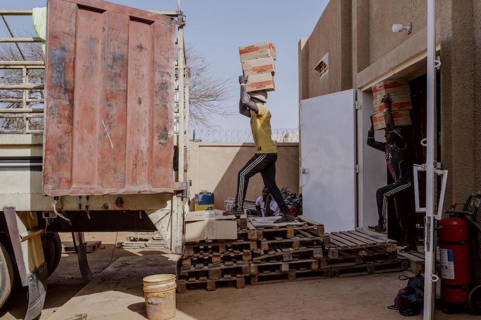 A man carries a box of nutritional supplementation on his head to a truck