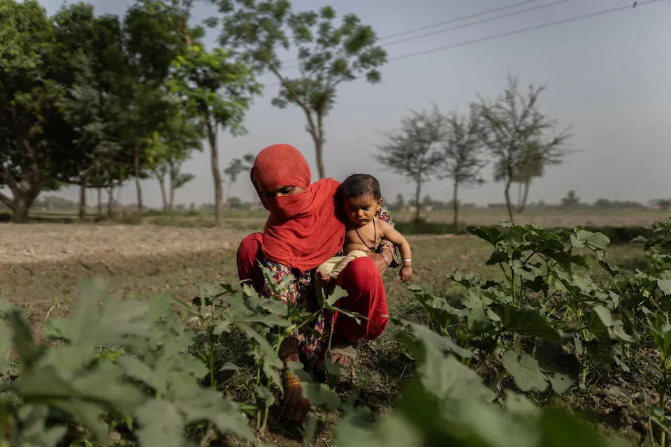 A mother holds her 6-month-old baby while working in the field in South Punjab, Pakistan.