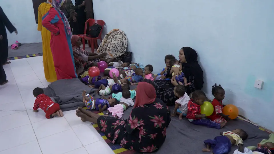 Children and their carers, relocated from Khartoum, rest inside a UNICEF-supported facility.