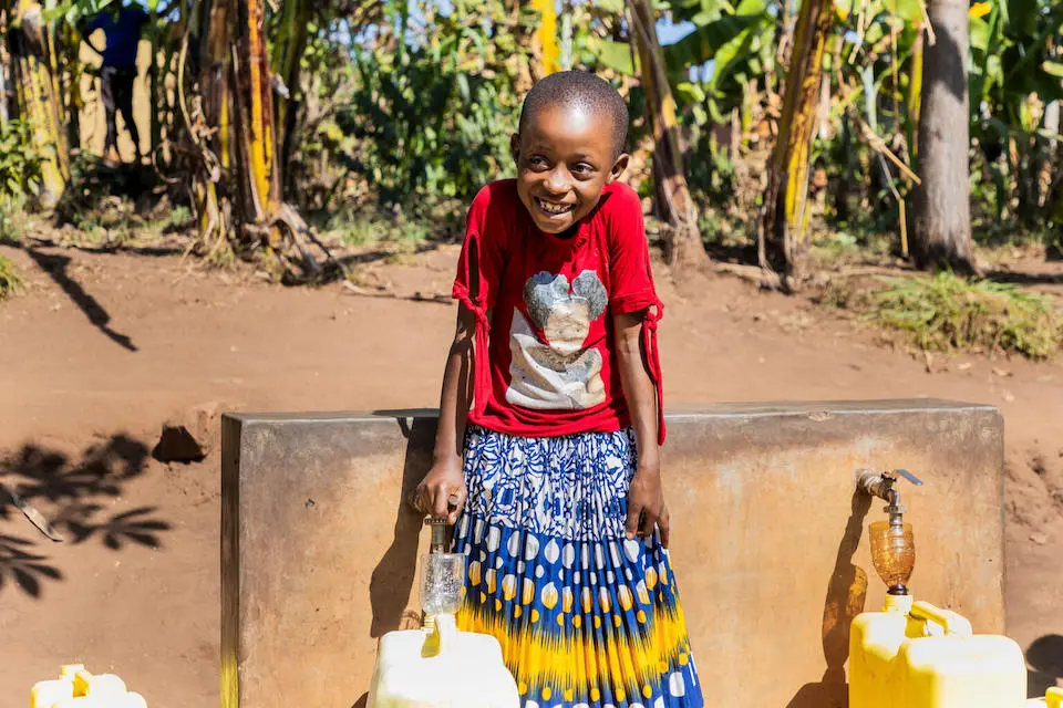 Eight-year-old Bonette fills water containers from taps that are part of a solar-powered water supply system in her neighborhood in Kigarama Sector, Kirehe District, Eastern Province of Rwanda.