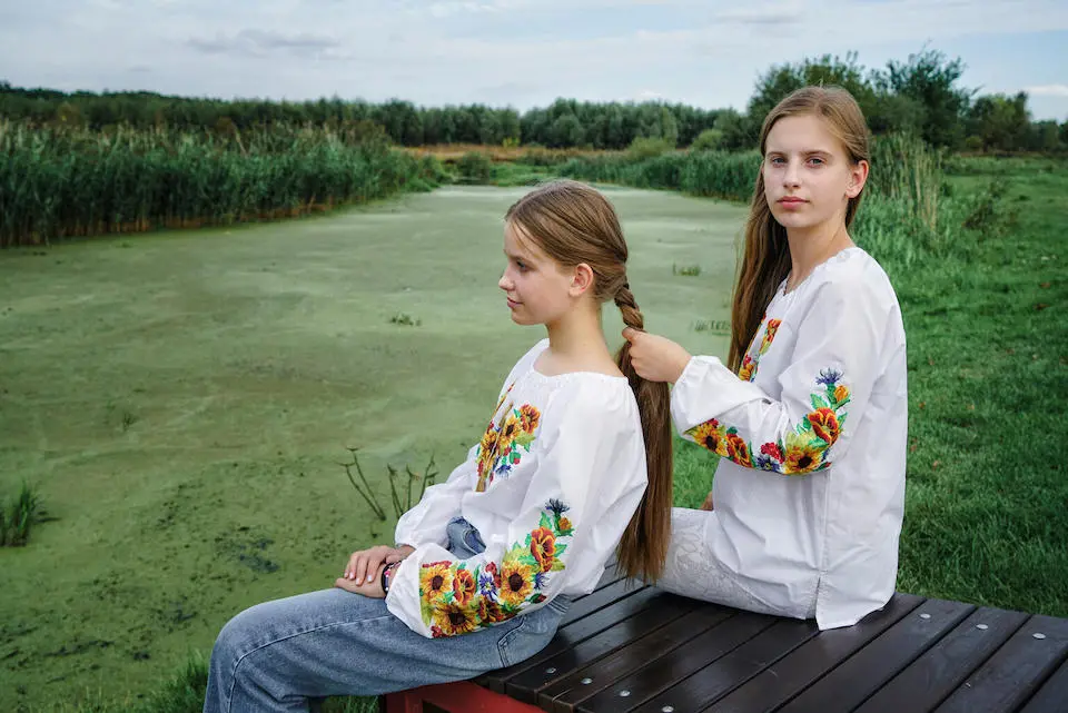 On Sept. 9, 2023, on the banks of the river in Horenka village near Kyiv, Ukraine, 14-year-old Nelya gazes into the distance while her 13-year-old sister Lilya braids her hair.