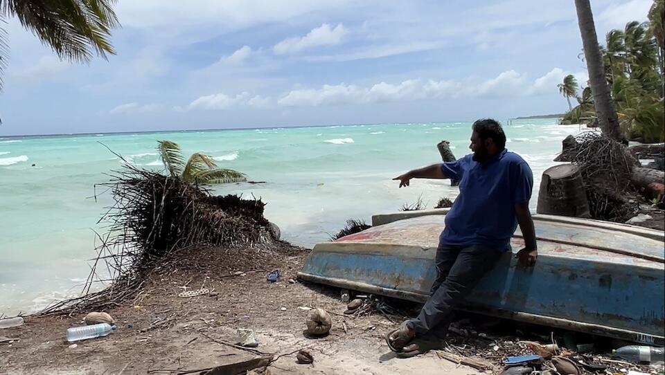 Maeed Zahir, Climate Resilience Consultant for UNICEF Maldives, points out telltale signs of beach erosion along the coast of Gan island in Laamu Atoll. Just moments before, a palm tree that had been leaning over the water from the edge of the land, its roots battered by waves, tipped over into the water.