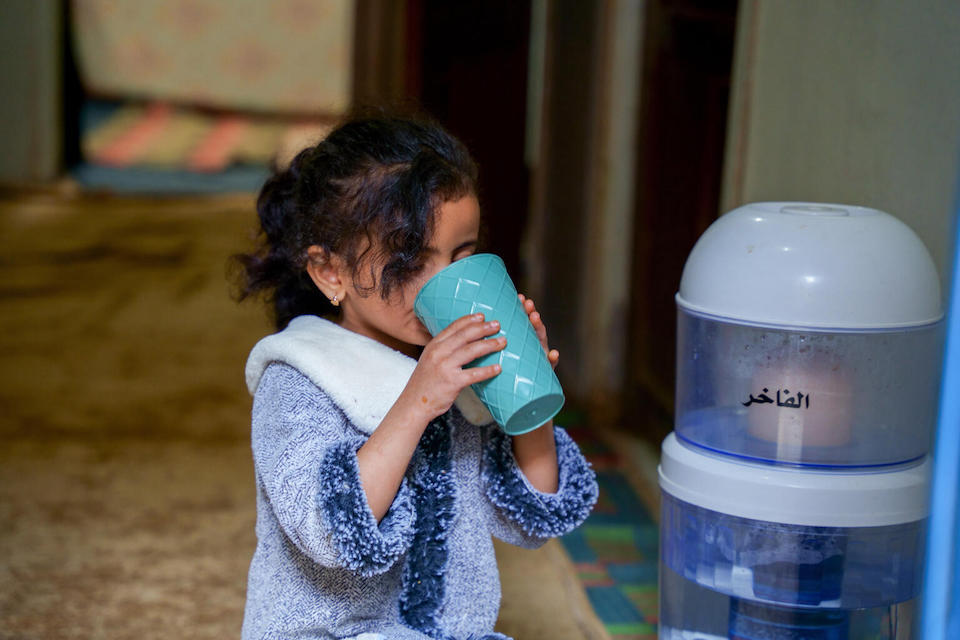 In Dhamar governorate, Yemen, a 7-year-old girl drinks water from a dispenser inside her home that is connected to a UNICEF-supported solar-powered system.
