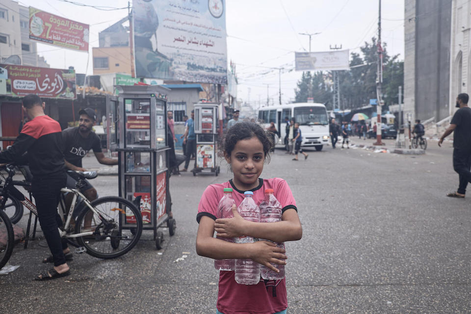 In the Gaza Strip, Salwa holds empty bottles on her way to fill them with drinking water for her family. 