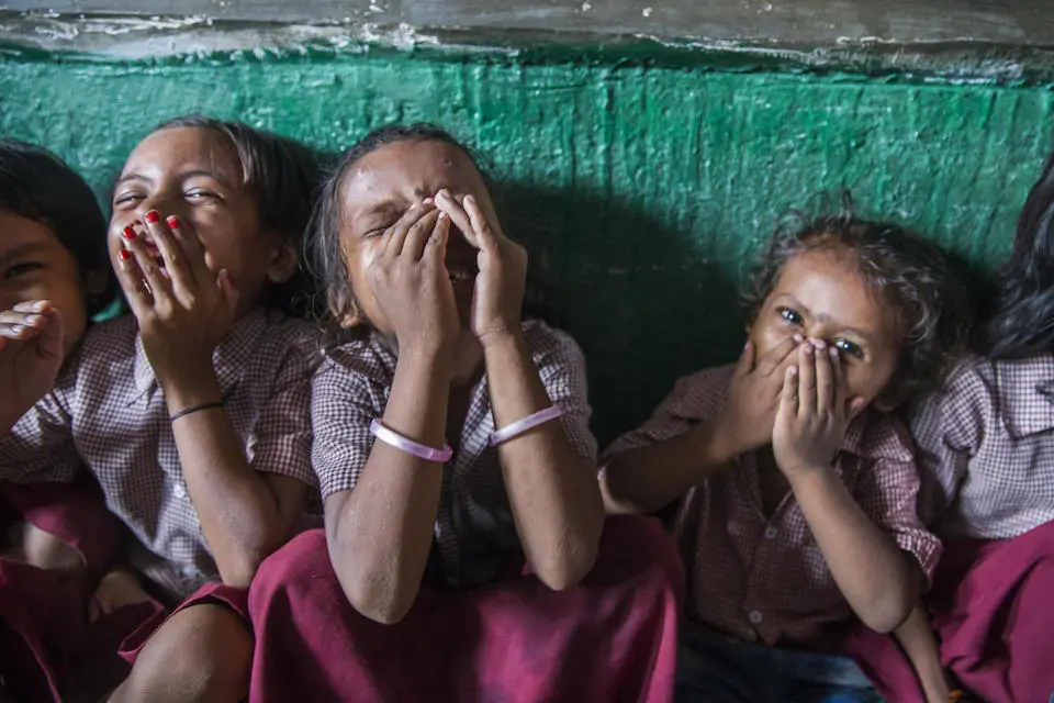 Girls hold hands over their laughing smiling mouths at a UNICEF-supported village school in Cherki, Sherghati block, Gaya district, Bihar state, India.