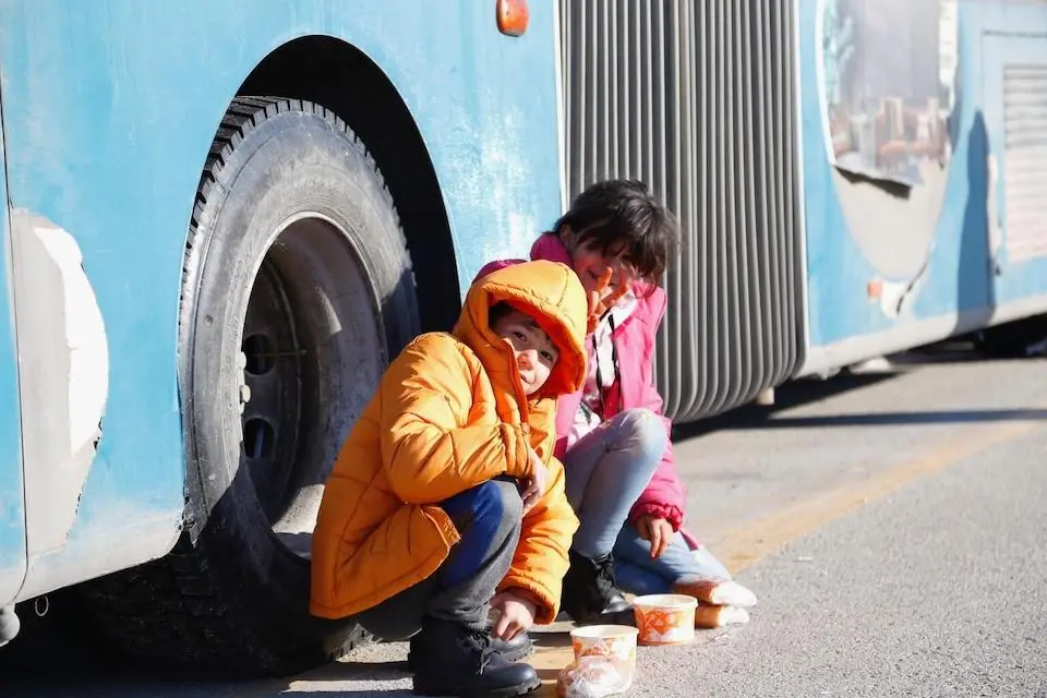In Feb. 2023 at the Intercity Bus Terminal in Malatya, Türkiye, children sit outside a bus being used as a temporary shelter for families displaced by a magnitude 7.7 earthquake.