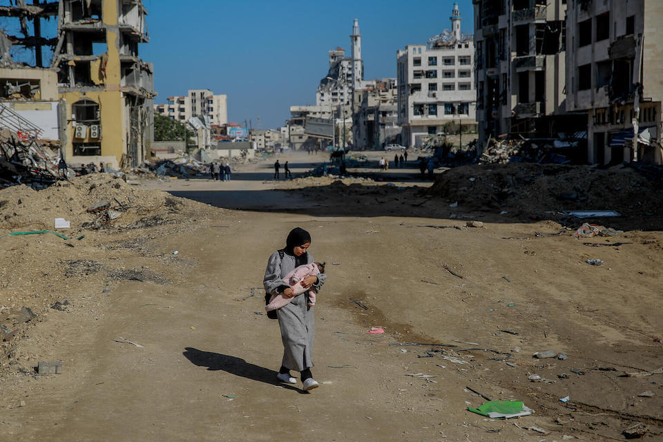 Salma, 29, carries her infant while walking along what remains of Rashid Street, west of Gaza City.