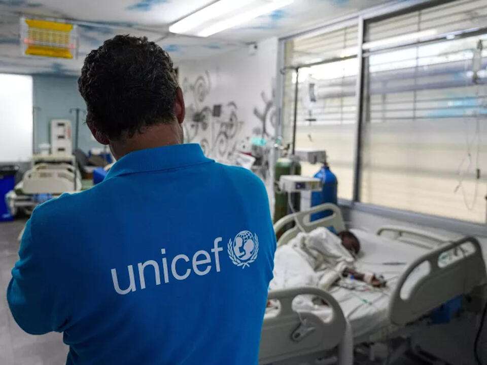 An injured child lies in a hospital bed in Port-au-Prince as a UNICEF staffer looks on.