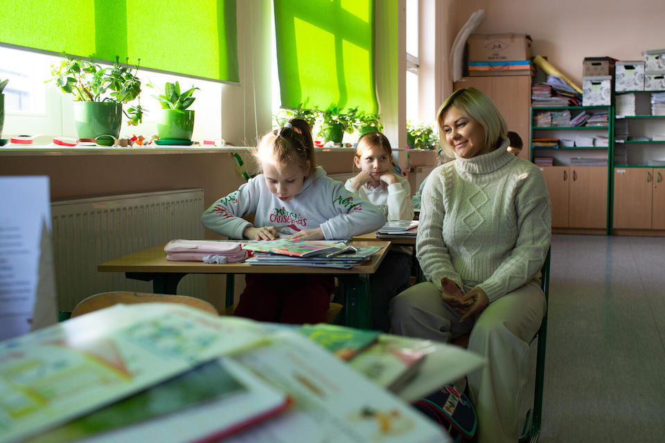 Students work with a teacher in a classroom in Poland. 