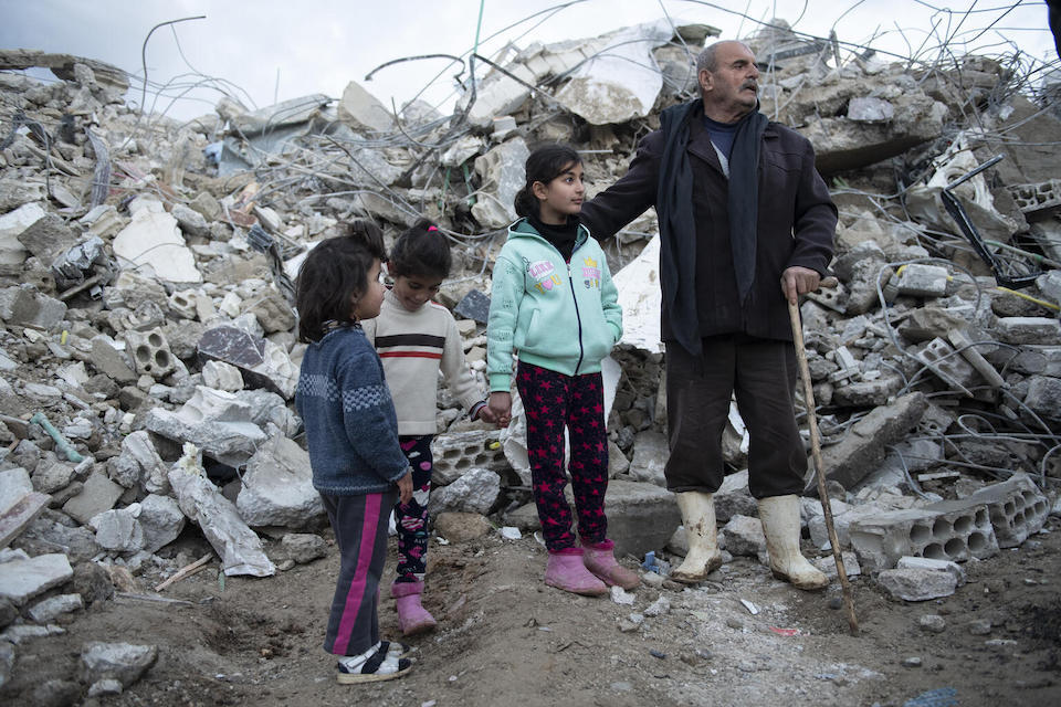 A family from Jableh district, Lattakia Governorate, in northwestern Syria, stands near their destroyed house, after a devastating earthquake hit their city on Feb. 5, 2023.